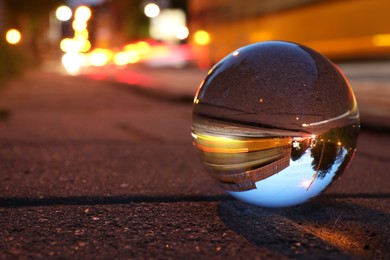 Photo of Beautiful city street, overturned reflection. Crystal ball on asphalt road at night. Space for text