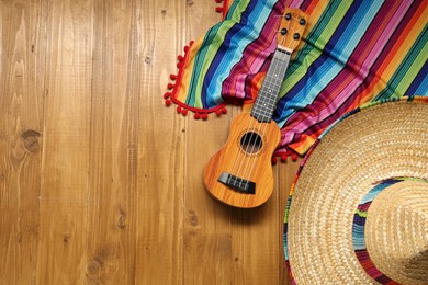 Mexican sombrero hat, guitar and colorful poncho on wooden background, flat lay. Space for text