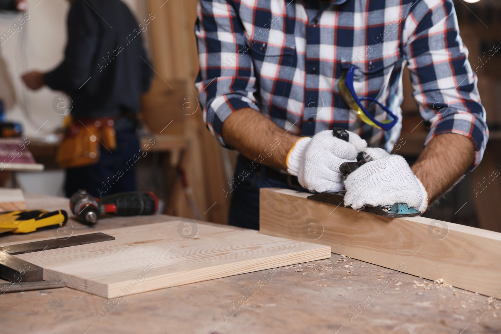 Photo of Professional carpenter grinding wooden plank with jack plane in workshop, closeup