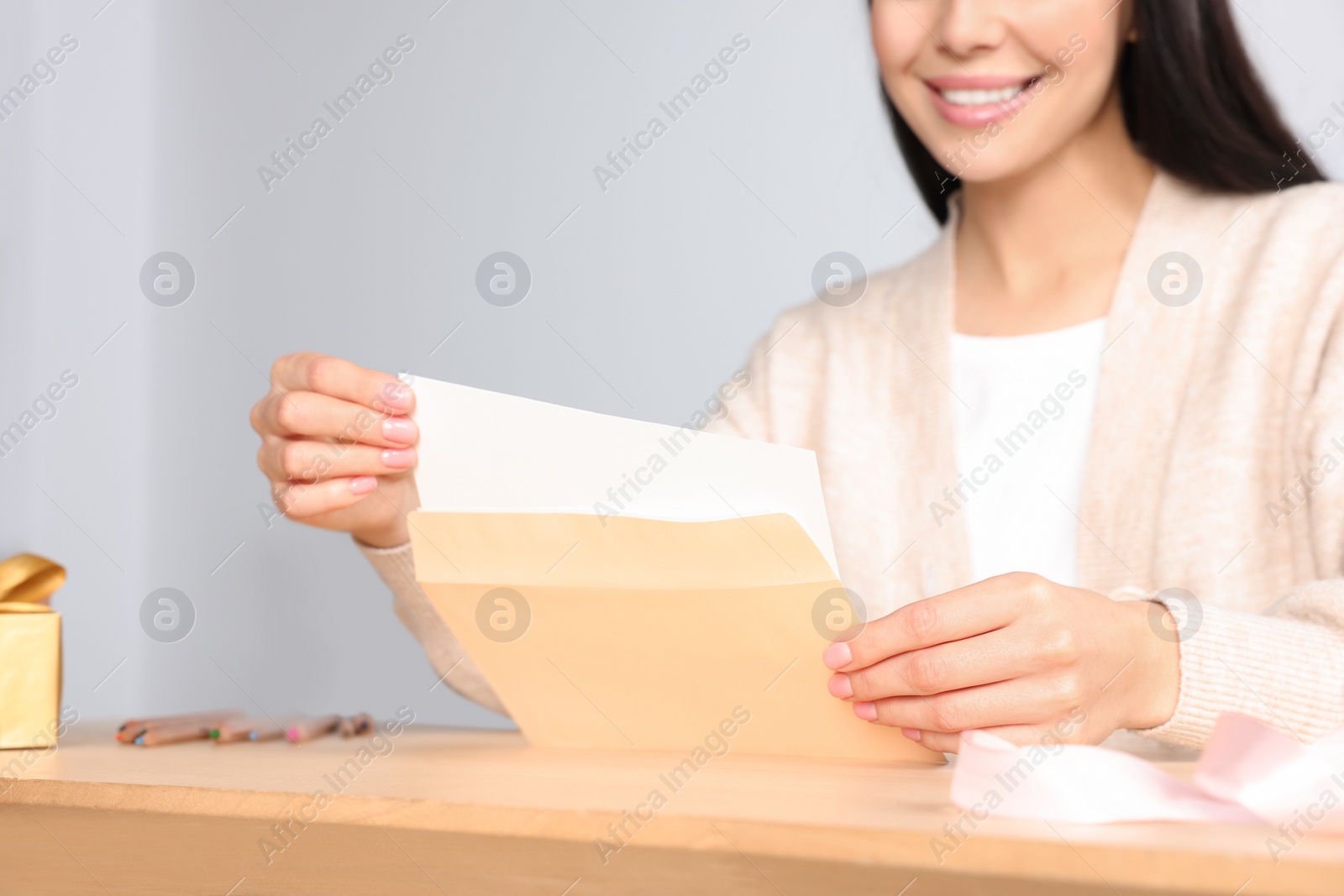 Photo of Happy woman holding greeting card at wooden table, closeup