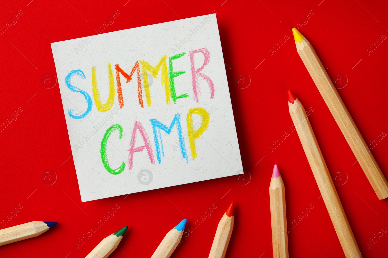 Photo of Paper with written text SUMMER CAMP and different pencils on color background, flat lay