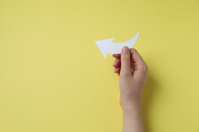 Photo of Woman holding curved paper arrow on yellow background, top view. Space for text