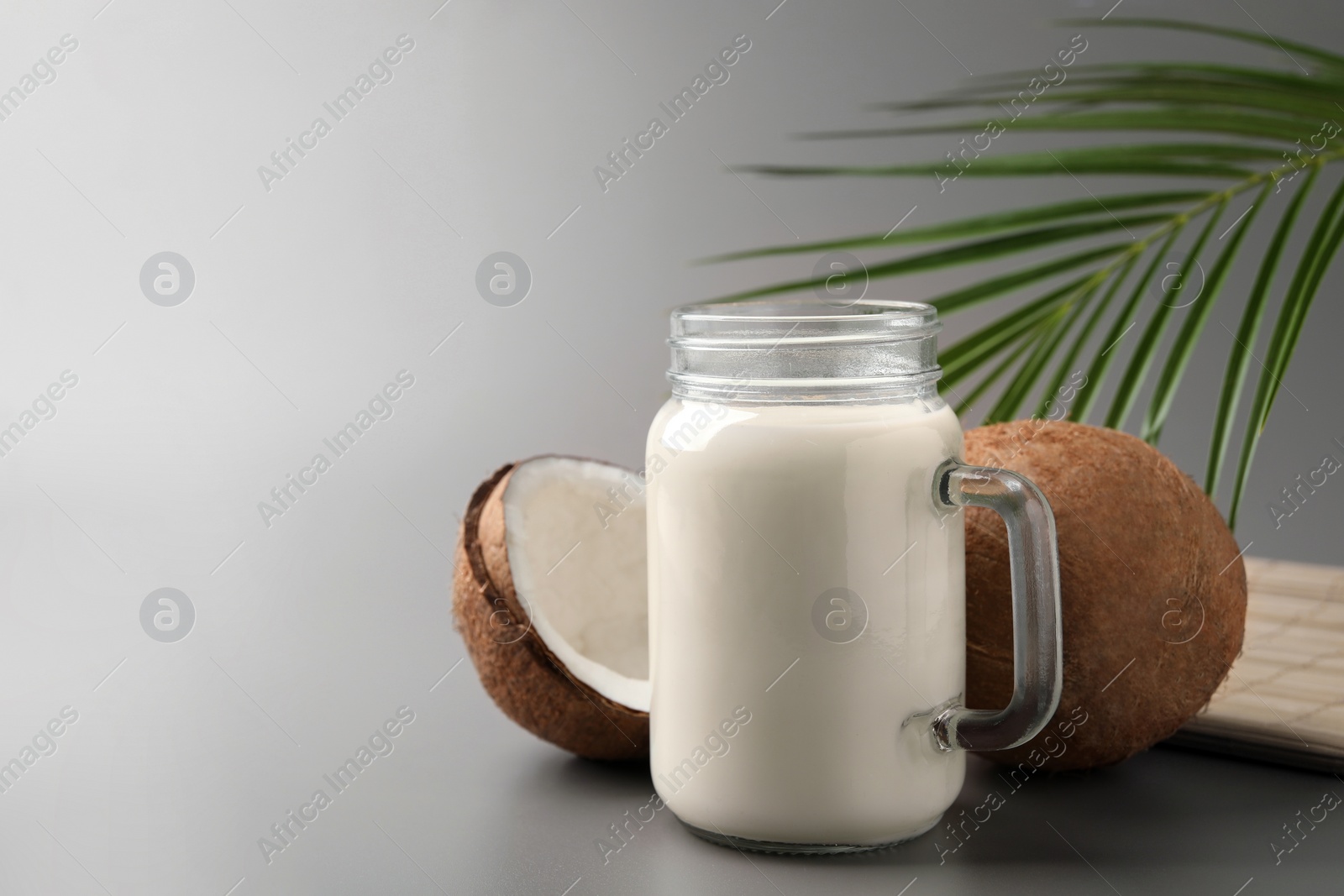 Photo of Mason jar of delicious vegan milk, coconuts and leaf on grey background. Space for text