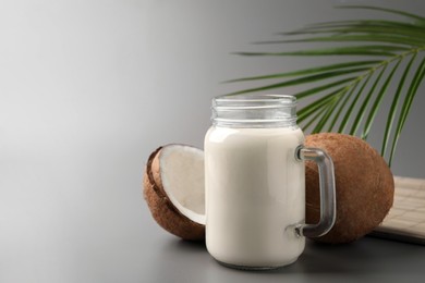 Photo of Mason jar of delicious vegan milk, coconuts and leaf on grey background. Space for text