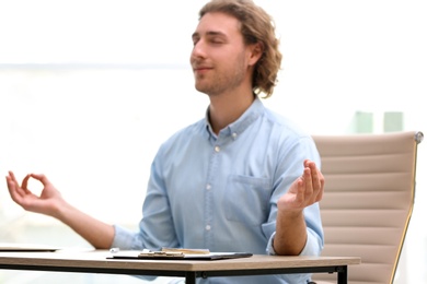 Young businessman meditating at table in office during break, space for text. Zen yoga