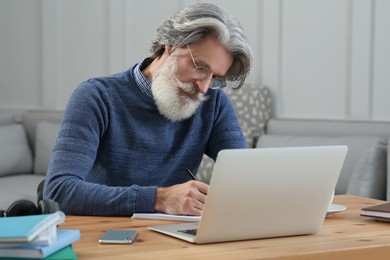 Middle aged man with laptop and notebook learning at table indoors