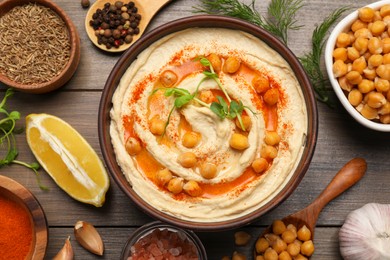 Photo of Delicious hummus with chickpeas and different ingredients on wooden table, flat lay