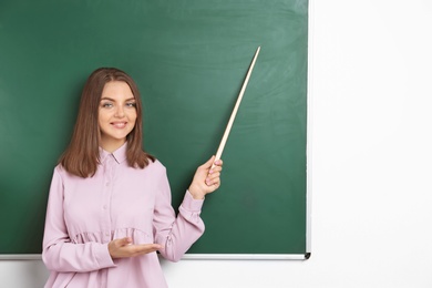 Photo of Portrait of female teacher with pointer near chalkboard in classroom