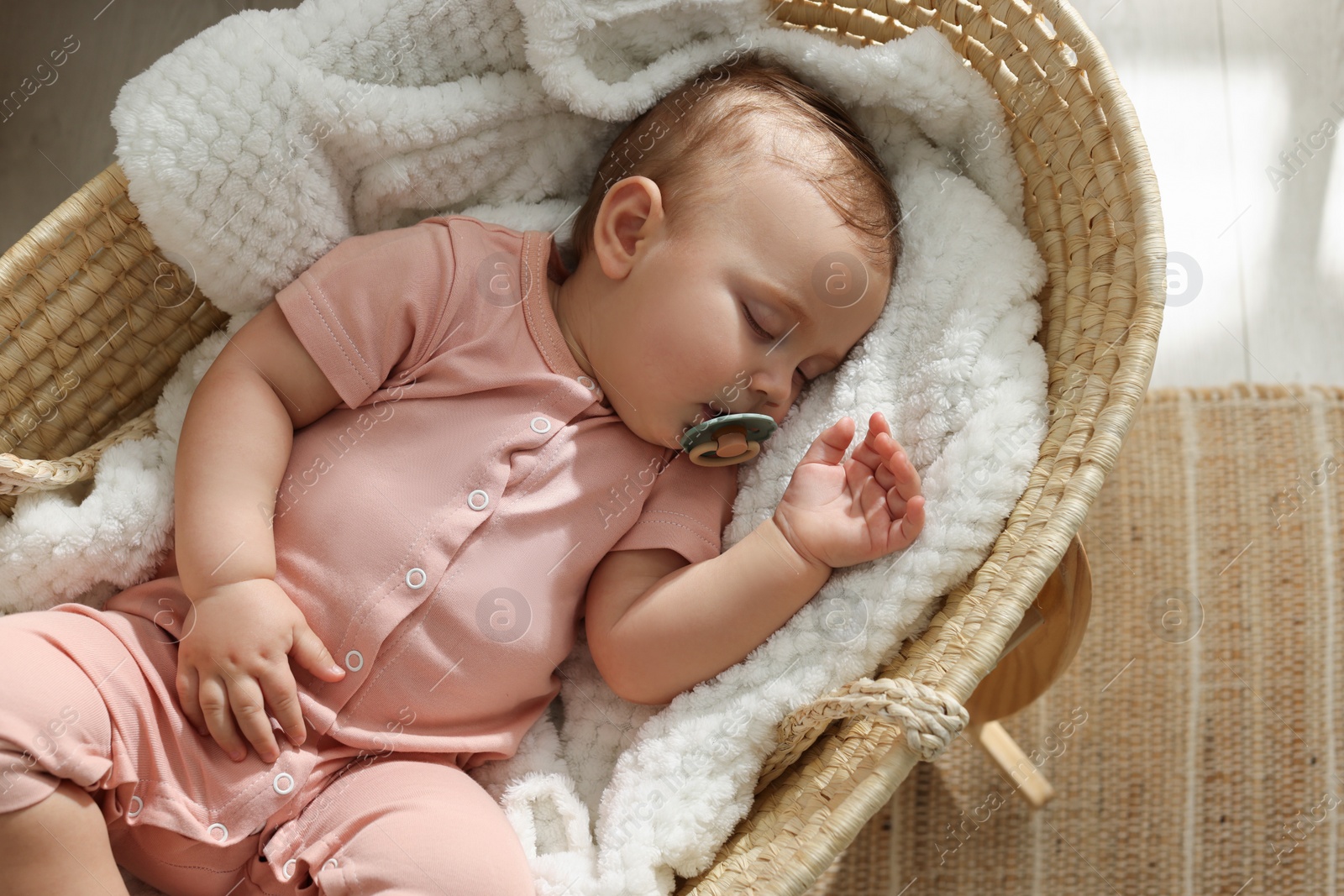 Photo of Cute little baby with pacifier sleeping in wicker crib at home, top view