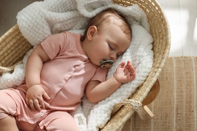 Cute little baby with pacifier sleeping in wicker crib at home, top view