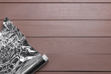 Roll of aluminum foil on wooden table, top view. Space for text