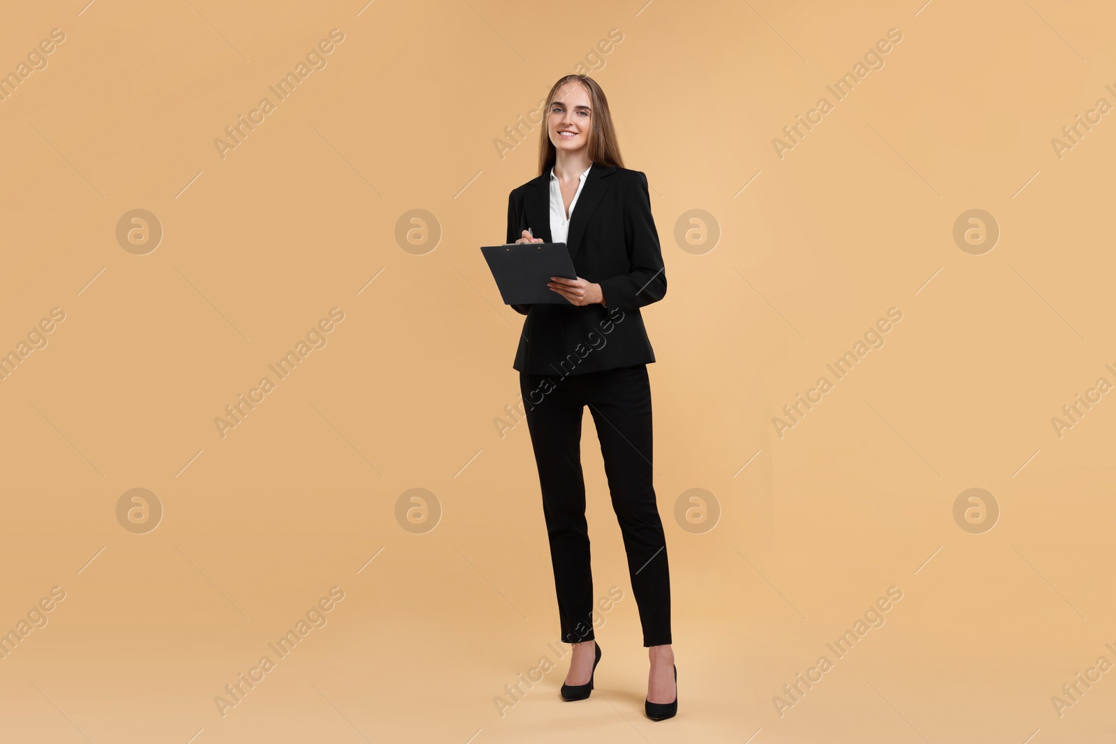 Photo of Happy young secretary with clipboard and pen on beige background