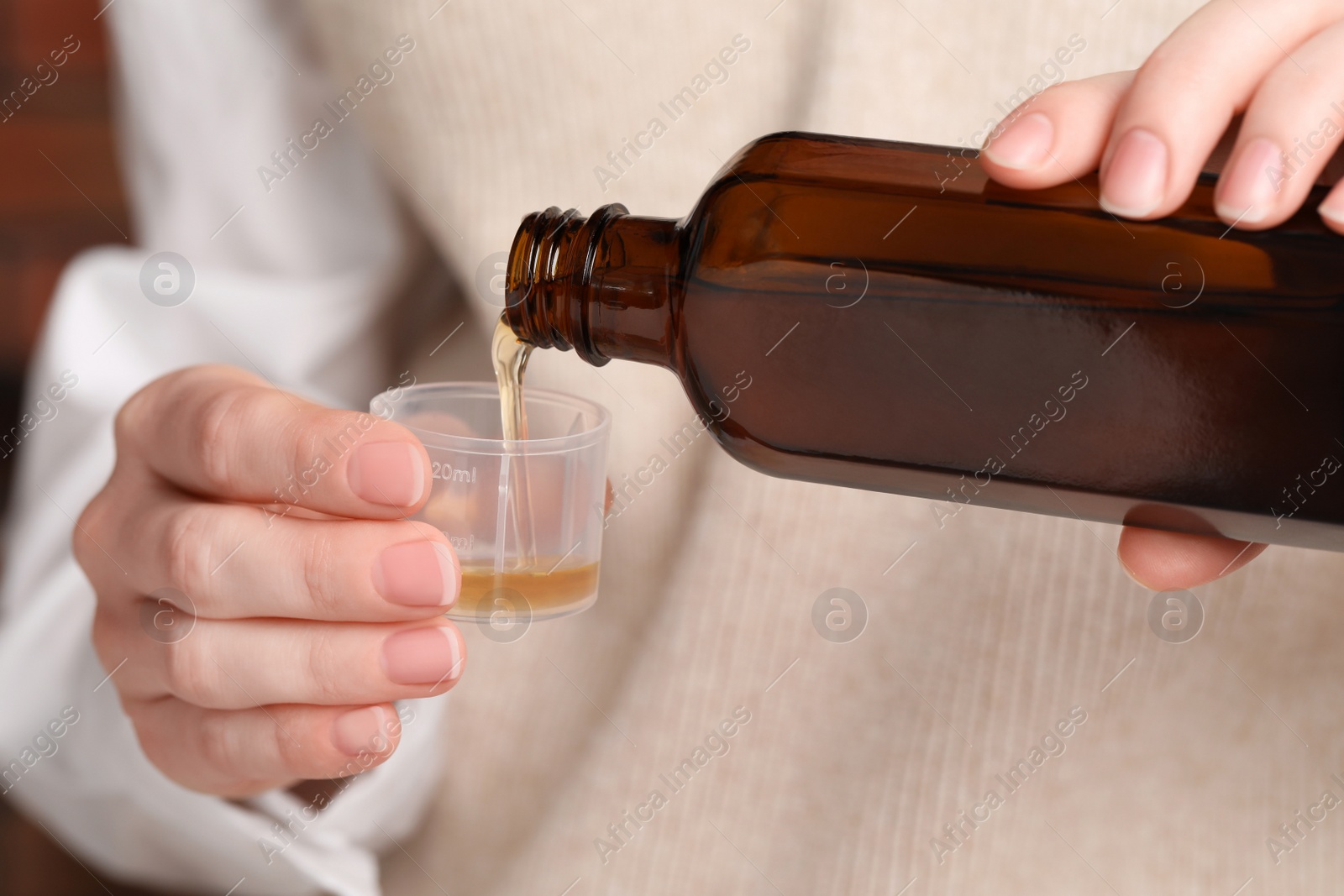 Photo of Woman pouring syrup from bottle into measuring cup, closeup. Cold medicine