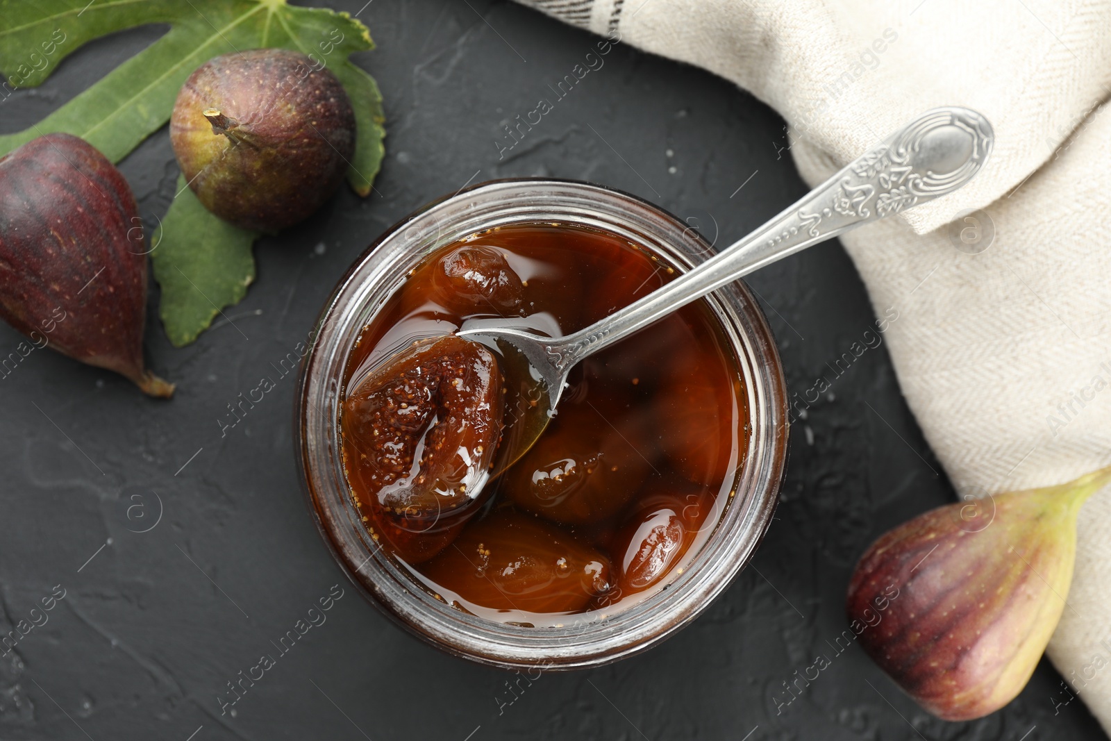 Photo of Jar of tasty sweet jam and fresh figs on black table, flat lay