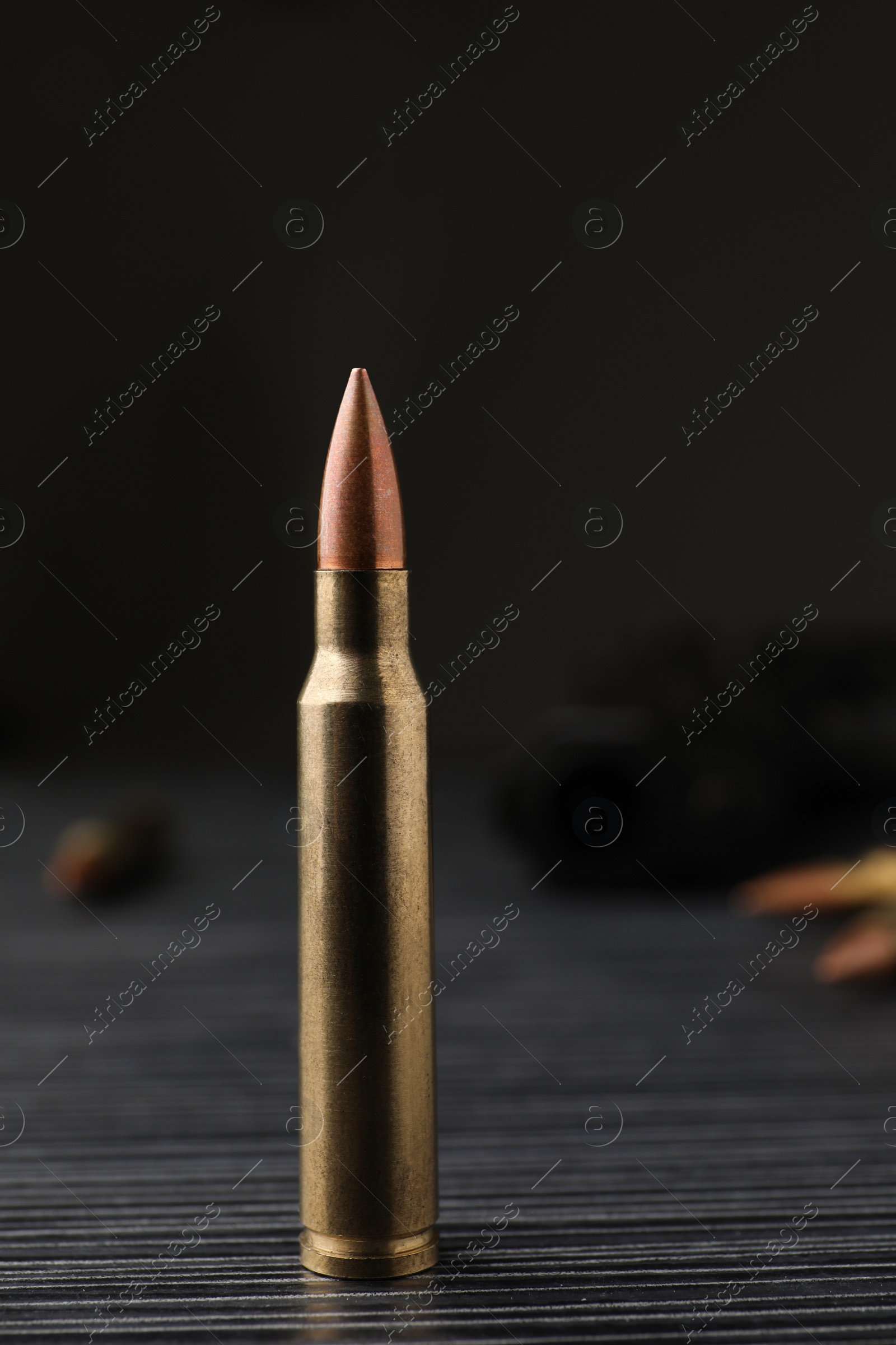 Photo of Bullet on black wooden table, closeup. Military ammunition