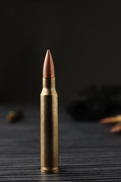 Photo of Bullet on black wooden table, closeup. Military ammunition