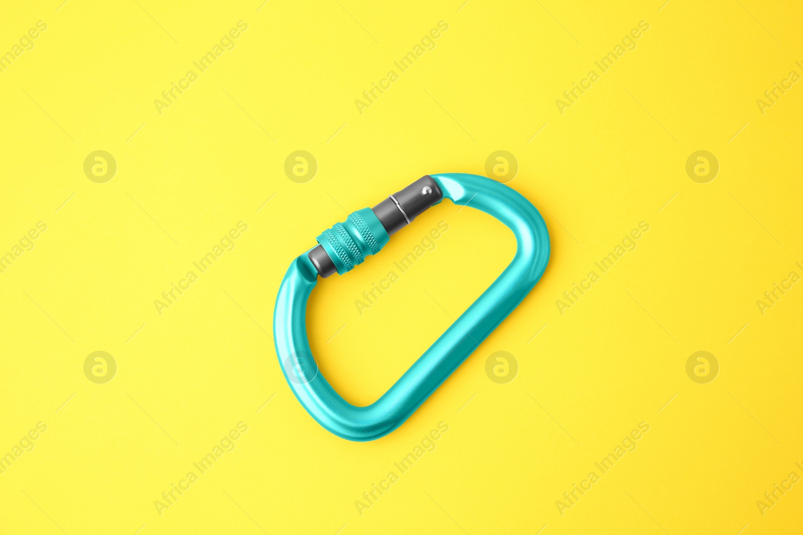 Photo of One light blue carabiner on yellow background, top view