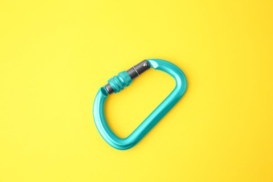 Photo of One light blue carabiner on yellow background, top view