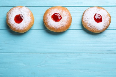 Photo of Hanukkah doughnuts with jelly and sugar powder on light blue wooden table, flat lay. Space for text