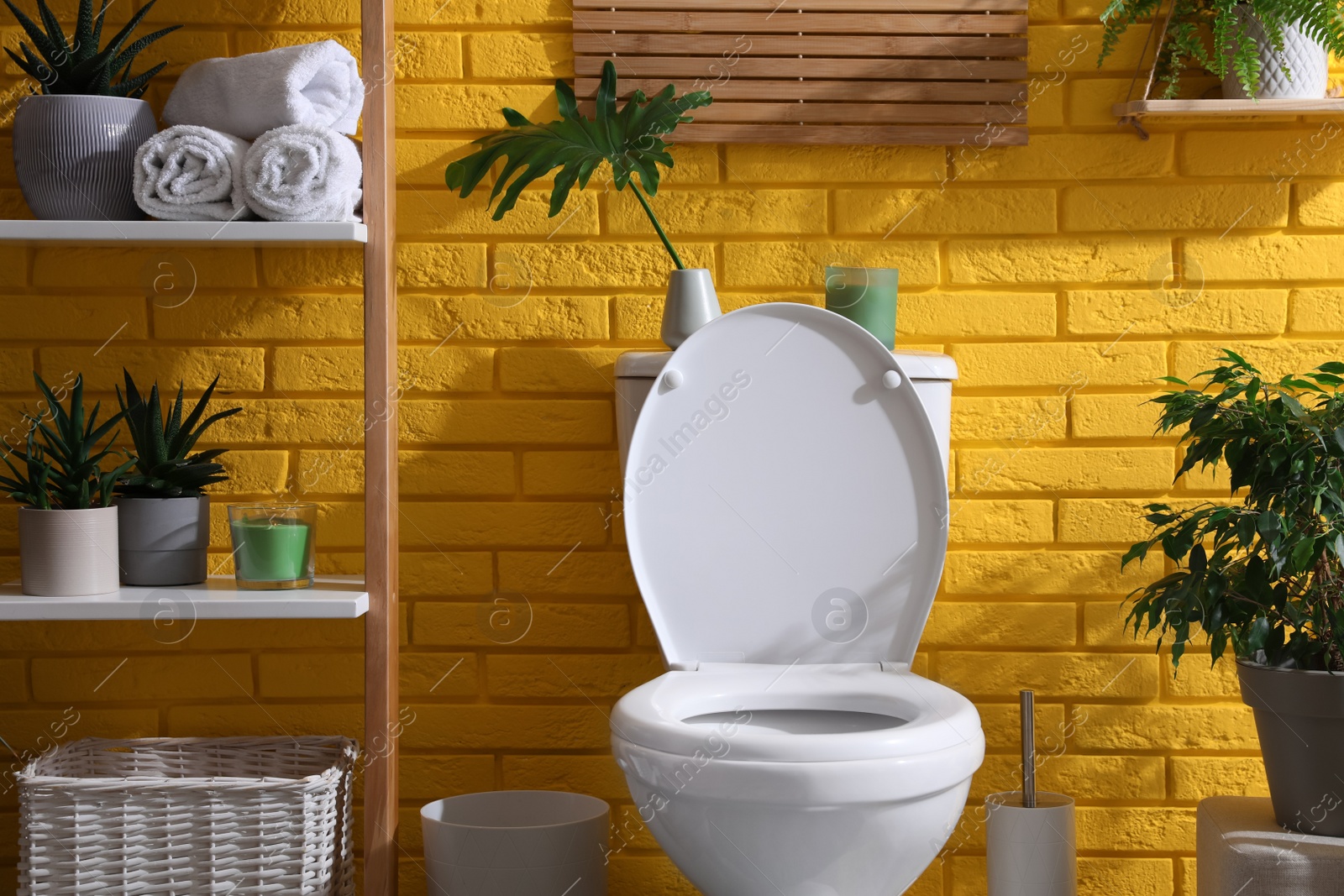 Photo of Stylish bathroom with toilet bowl and green plants near yellow brick wall. Interior design