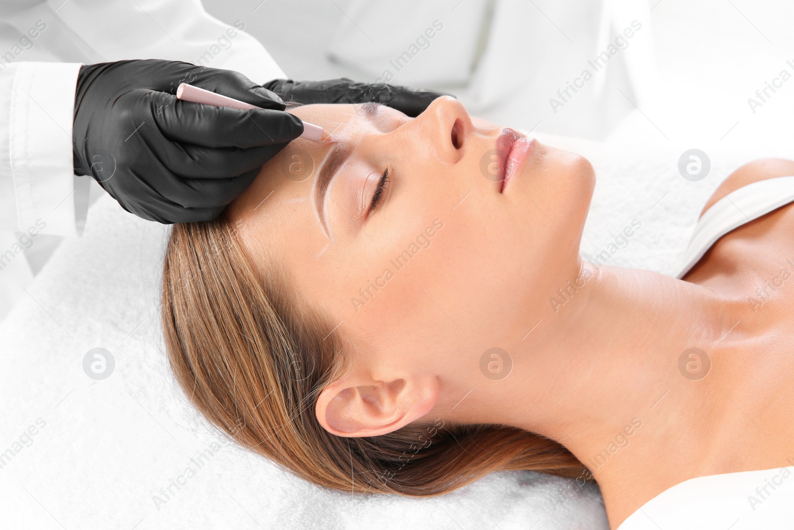 Photo of Young woman undergoing eyebrow correction procedure in salon