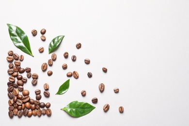 Photo of Fresh green coffee leaves and beans on light background, flat lay. Space for text