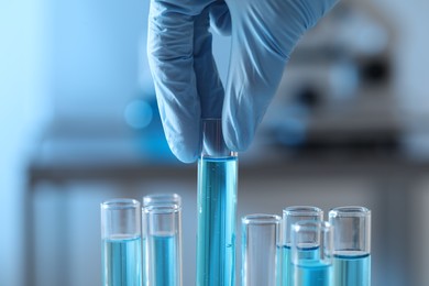 Photo of Scientist taking test tube with light blue liquid in laboratory, closeup