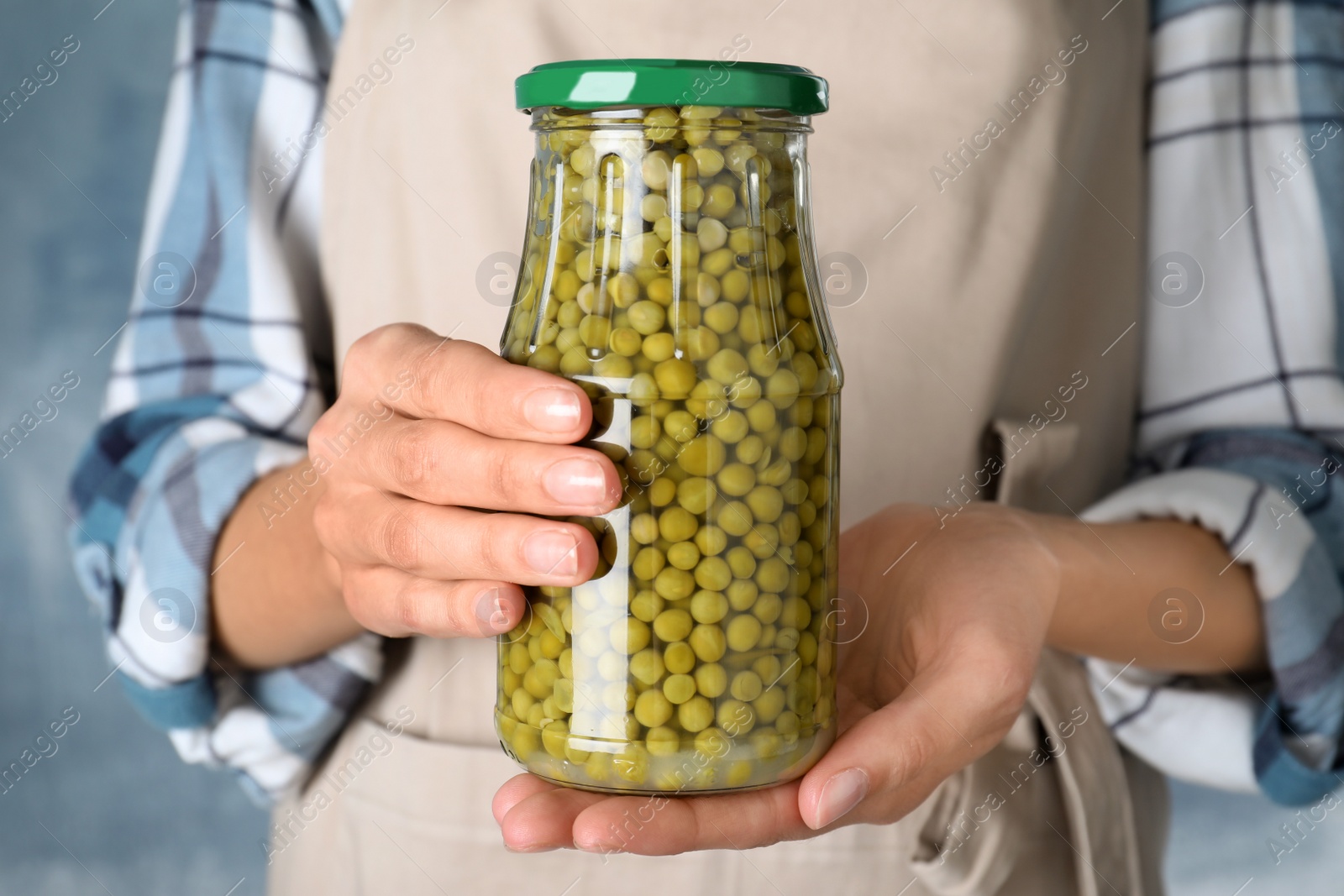Photo of Woman holding jar with pickled peas against blue background, closeup