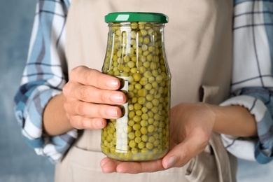 Woman holding jar with pickled peas against blue background, closeup