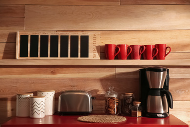 Photo of Modern coffeemaker and toaster on red table near wooden wall