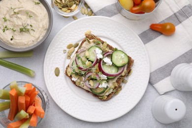 Photo of Tasty vegan sandwich with cucumber, onion, hummus and pumpkin seeds on light grey table, flat lay