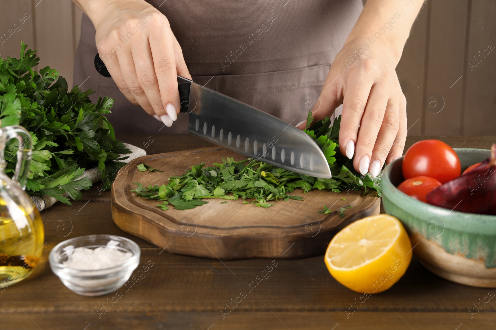 Photo of Woman cutting fresh parsley at wooden table, closeup
