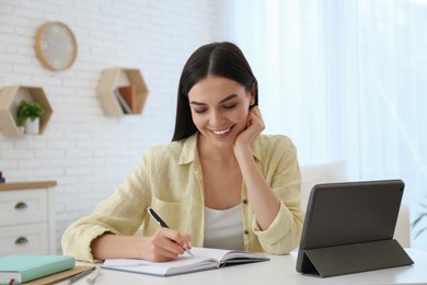 Photo of Young woman taking notes during online webinar at table indoors