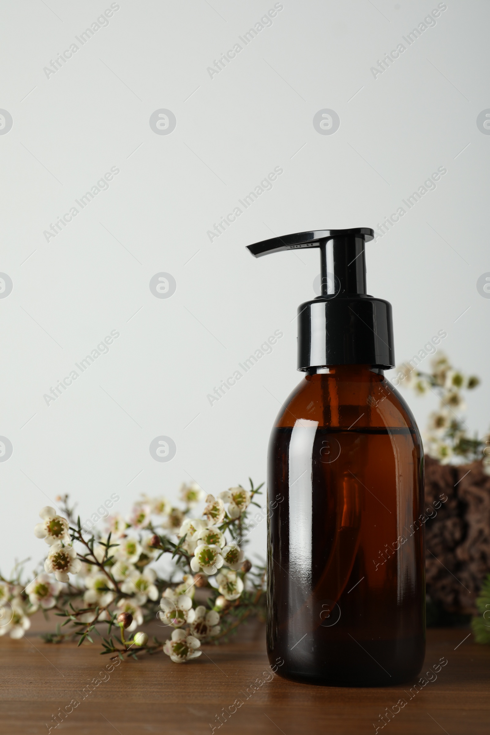 Photo of Bottle of hydrophilic oil and beautiful flowers on wooden table