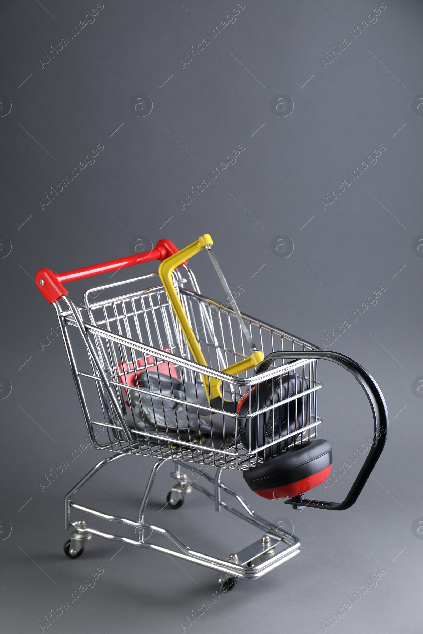 Photo of Small shopping cart with hacksaw, gloves and headphones on grey background