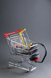 Small shopping cart with hacksaw, gloves and headphones on grey background