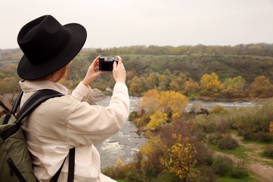 Photo of Traveler with backpack taking photos near mountain river. Autumn vacation