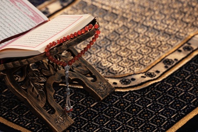 Photo of Rehal with open Quran and prayer beads on Muslim prayer mat. Space for text