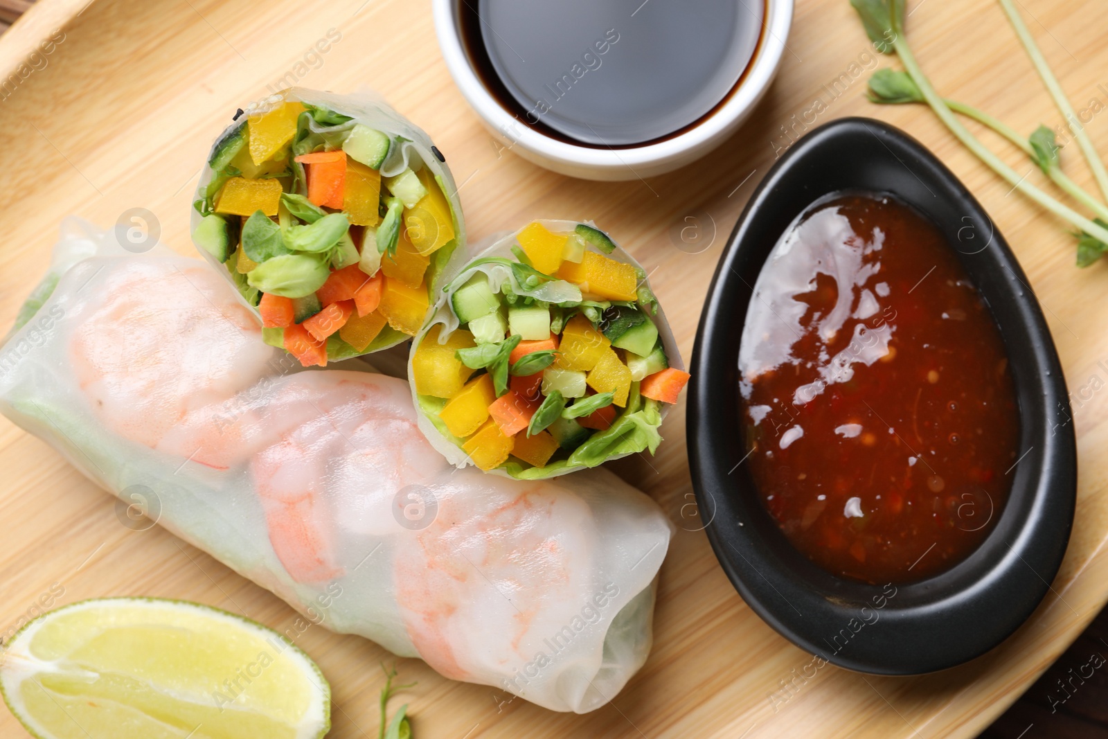 Photo of Tasty spring rolls and sauces on wooden plate, top view