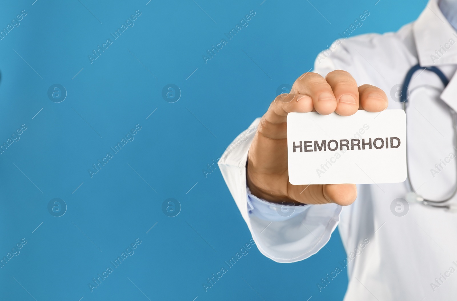 Photo of Doctor holding business card with word HEMORRHOID on blue background, closeup. Space for text