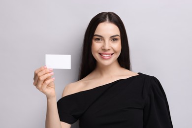 Happy woman holding blank business card on light grey background