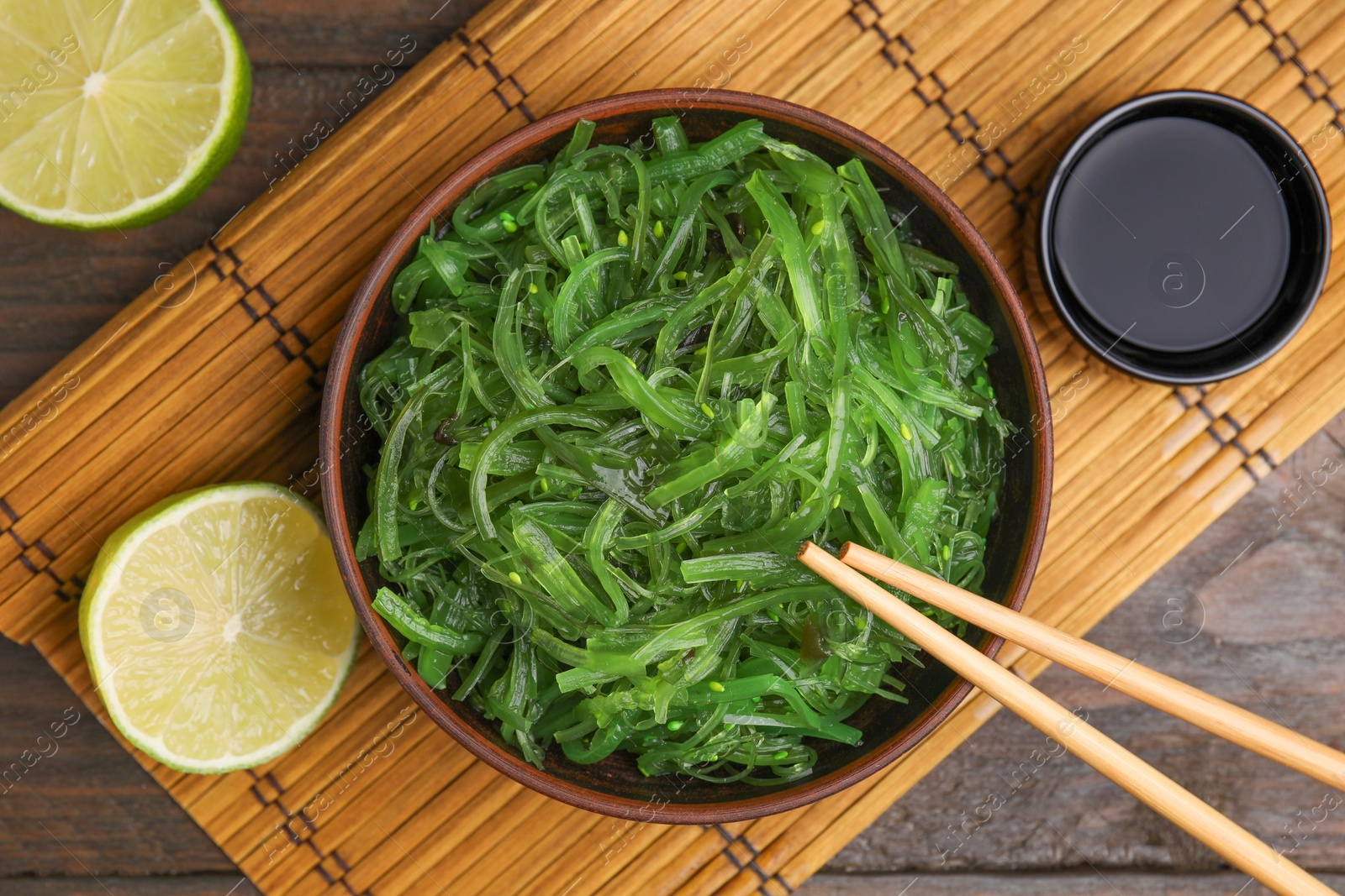 Photo of Tasty seaweed salad in bowl served on wooden table, flat lay