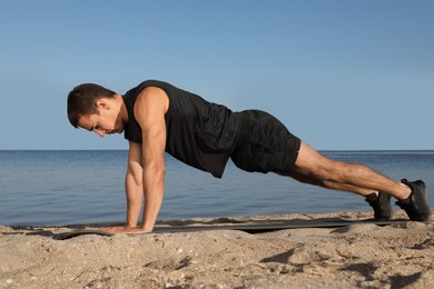 Sporty man doing straight arm plank exercise on beach