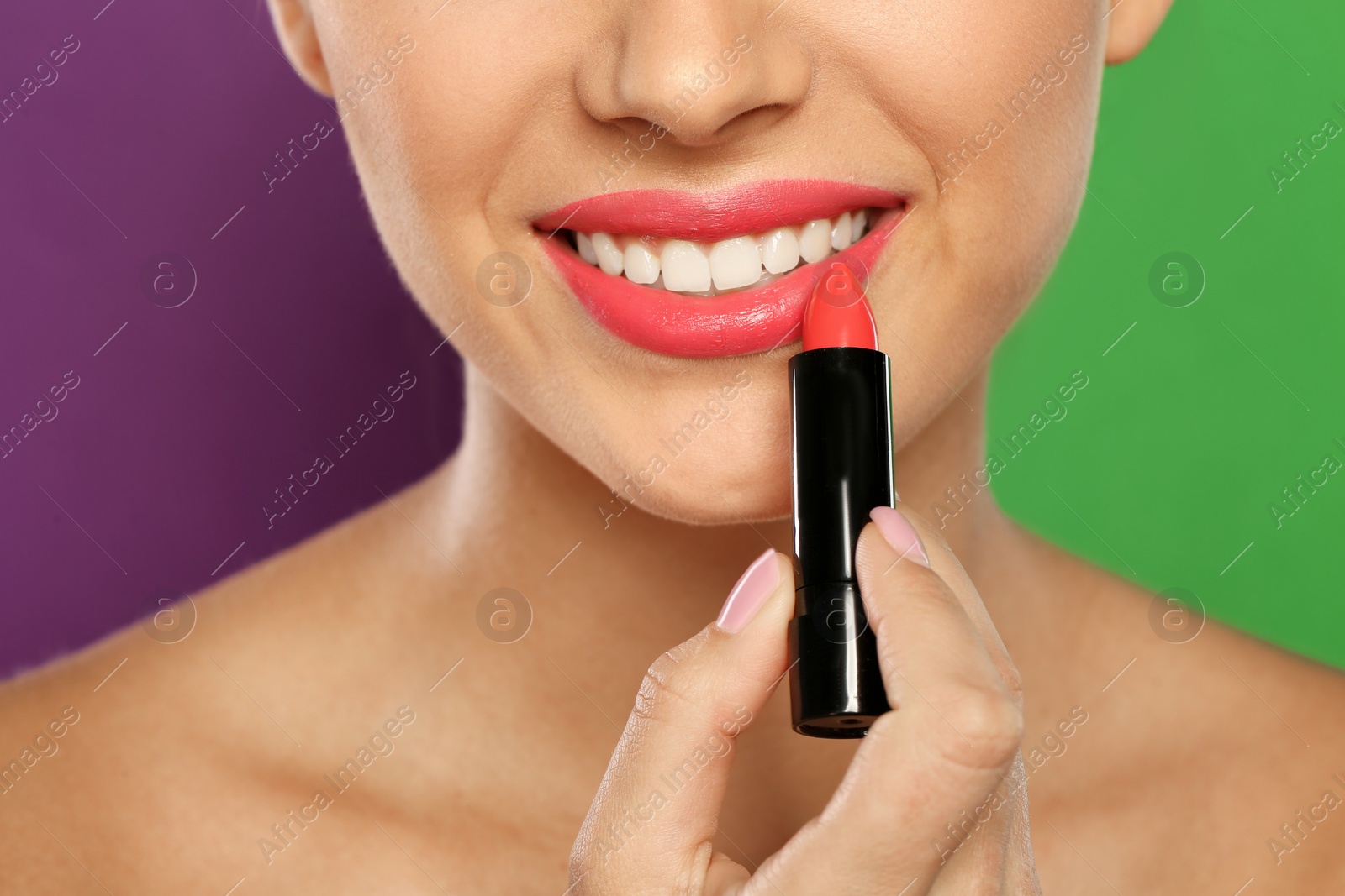 Photo of Young woman applying lipstick on color background, closeup