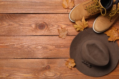 Hat, dry leaves and boots on wooden background, flat lay with space for text. Autumn season