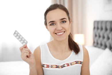 Young woman holding blister with vitamin pills indoors