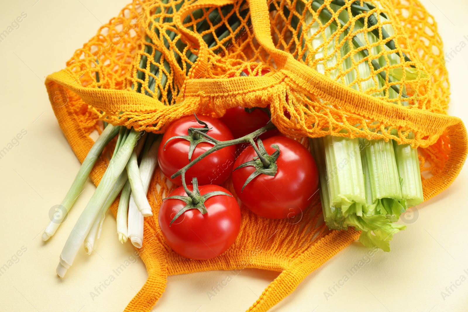 Photo of String bag with different vegetables on beige background, closeup