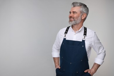 Photo of Happy man wearing kitchen apron on grey background. Mockup for design