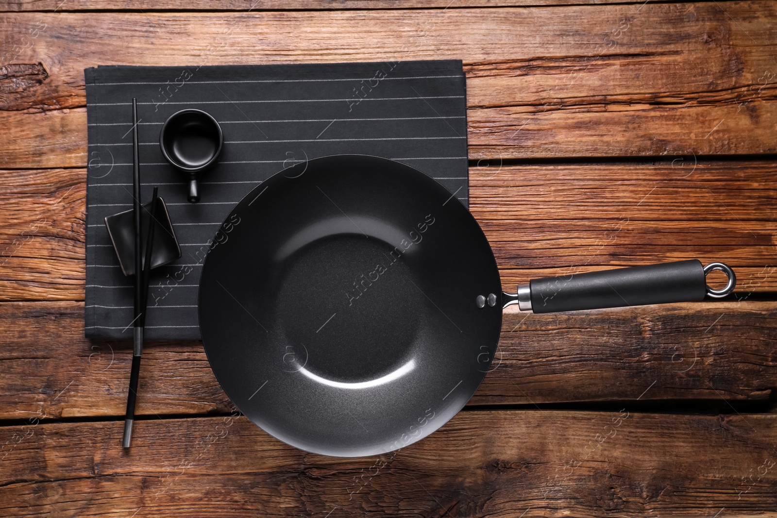 Photo of Empty iron wok, sauce bowl and chopsticks on wooden table, flat lay