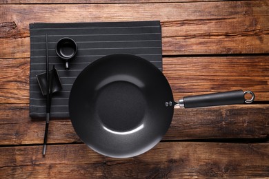 Photo of Empty iron wok, sauce bowl and chopsticks on wooden table, flat lay